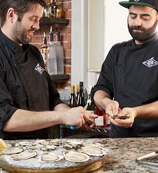 Two men shucking oysters at an oyster bar Two men shucking oysters at an oyster bar